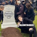 Paleontologist kneeling and smiling next to a tombstone that reads DINOSAURS HERRENDOUSLY DIED IN THE PAST